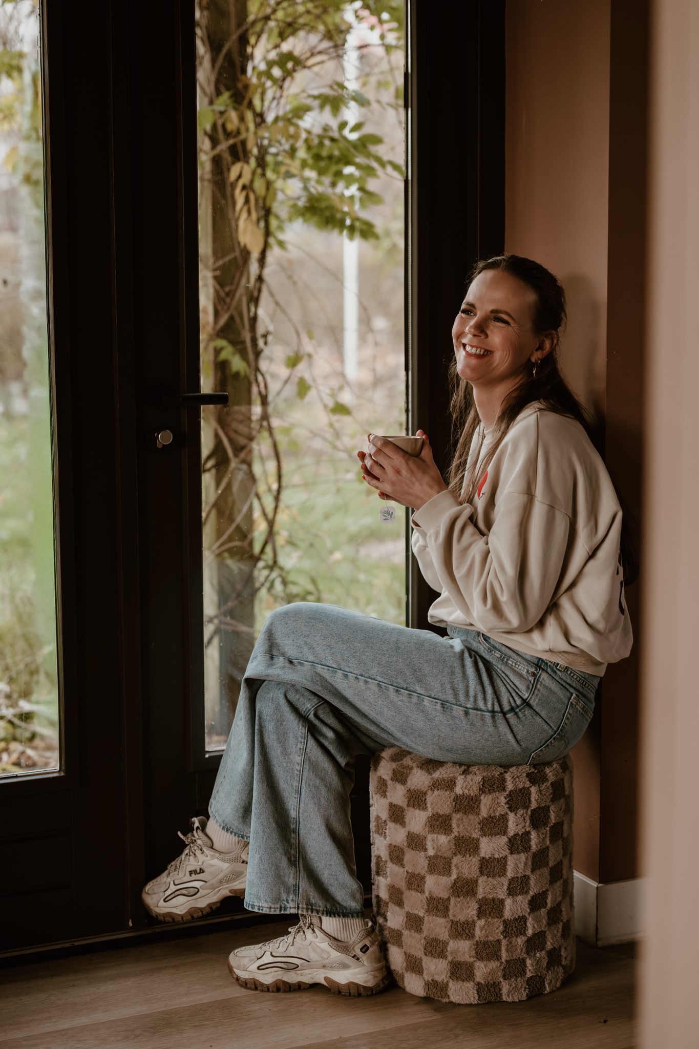 Margriet Appelo, lachend met een kop koffie bij het raam